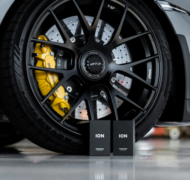 Close-up of a Porsche GT3 wheel with yellow brake calipers and Ceramic Pro ION product boxes in the foreground.